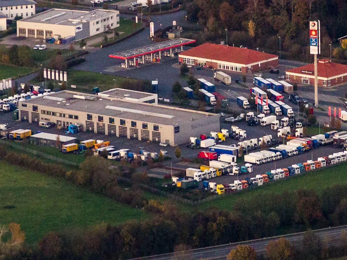 Rows of parked tractors and trailers of different types at a motorway truck stop, seen from the air