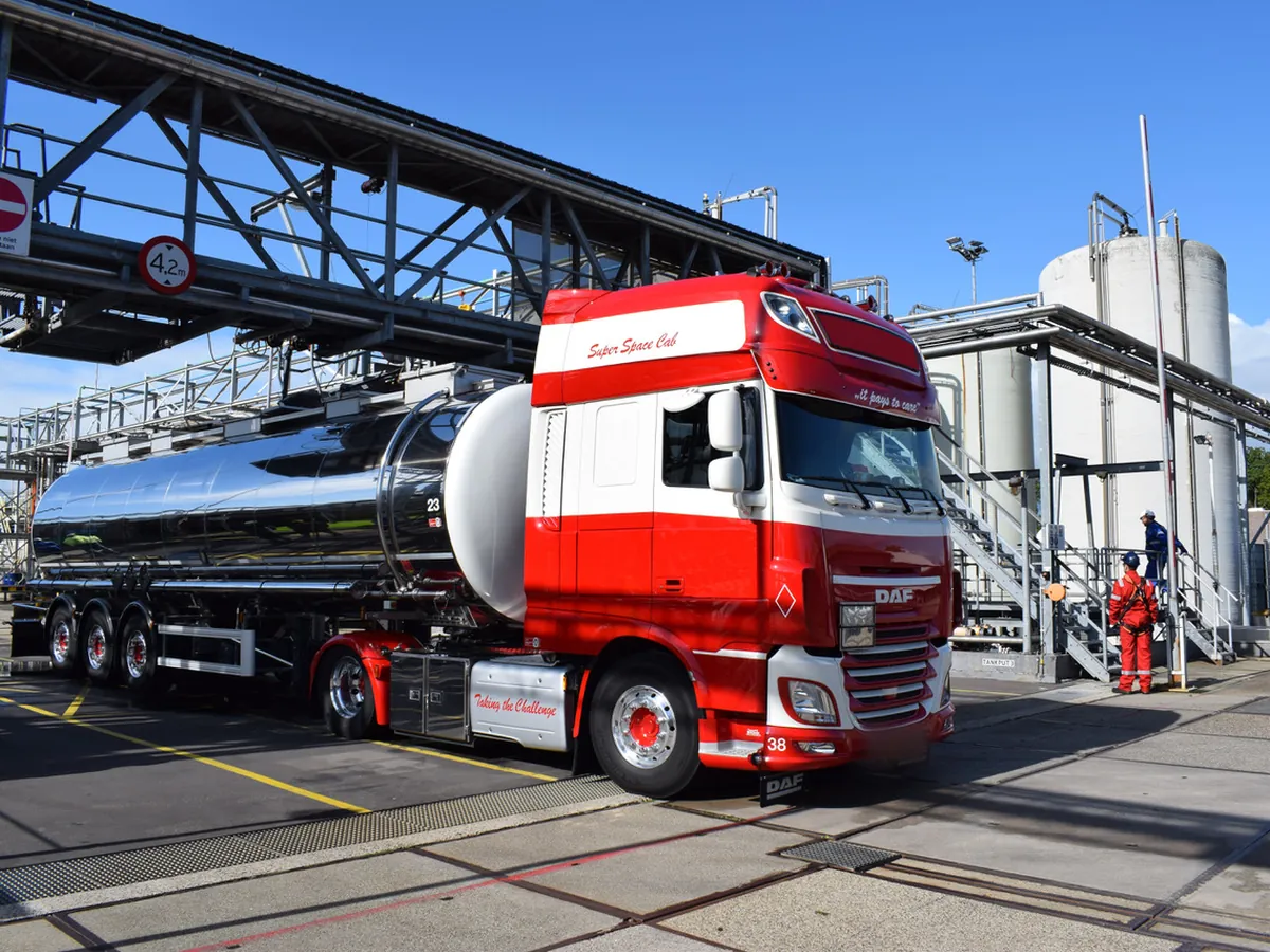 Tankwagen onder de laadbrug van een chemische fabriek, met een operator in beschermende kleding ernaast