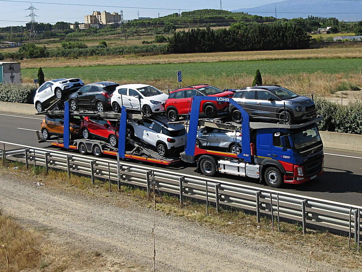 A car transporter carrying eleven cars on a motorway, the shared truck a dealer's own driver competes with