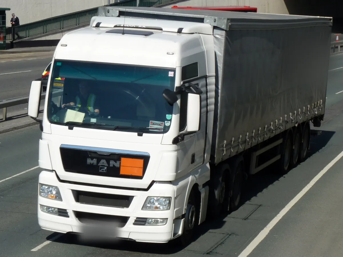 Planen-Lkw mit neutraler orangefarbener ADR-Warntafel am Kühlergrill, verpacktes Gefahrgut unterwegs