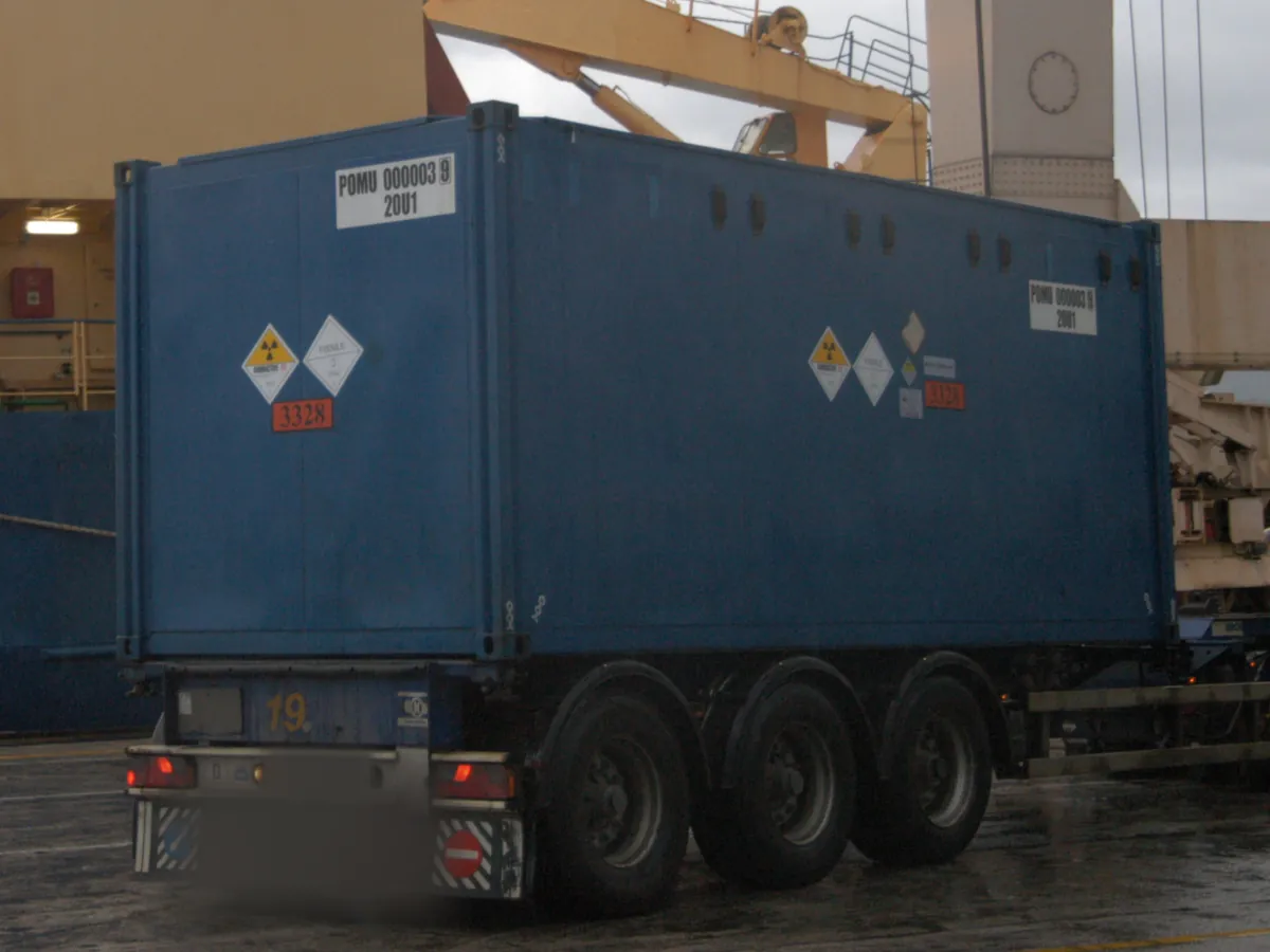 Container mit Gefahrzetteln der Klasse 7 und der UN-Nummer 3328 auf einem Sattelauflieger im Hafen Koper