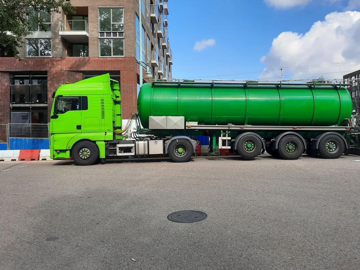 Tankoplegger achter een groene trekker in een straat in Amsterdam